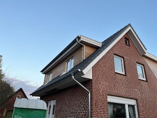 Backsteinhaus nach Dacherneuerung mit dunklem Satteldach und neuer Dachentwässerung