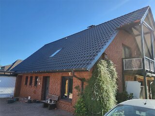 Saniertes Satteldach mit dunklen Dachziegeln und Dachfenster auf einem Backsteinhaus