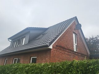 Backsteinhaus mit saniertem dunklem Ziegeldach und Dachgaube