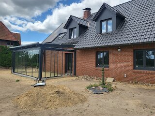 Backsteinhaus nach Dachsanierung mit dunkler Dacheindeckung, zwei Gauben und angebautem Glaswintergarten