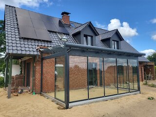 Saniertes Dach eines Backsteinhauses mit dunklen Dachziegeln, Dachgauben, Photovoltaikanlage und Glaswintergarten