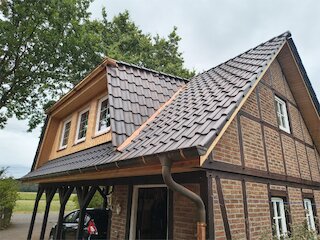 Fachwerkhaus nach Dachsanierung mit dunklem Ziegeldach und neuer Holzgaube