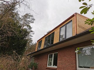 Hausaufstockung mit waagerechter Holzfassade und großen Fenstern auf einem Backsteinhaus