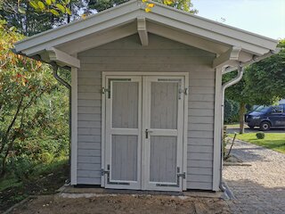 Grau gestrichenes Gartenhaus aus Holz mit Satteldach und zweiflügeliger Tür