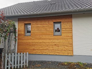 Waagerechte Holzfassade an einem Wohnhaus mit zwei eingefassten Fenstern