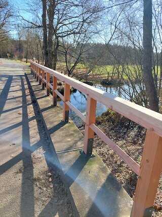 Langes Geländer aus Holz entlang eines befestigten Fußwegs im Park