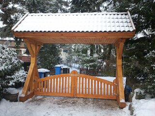 Überdachte Holzschaukel mit Sitzbank in einem verschneiten Garten