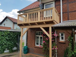 Balkon aus naturbelassenem Holz mit Stützen und Geländer an einem Backsteinhaus