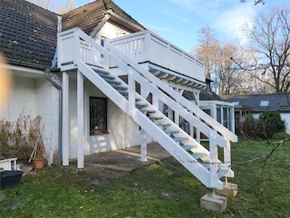 Weißer Holzbalkon mit Außentreppe und Geländer an einem Wohnhaus