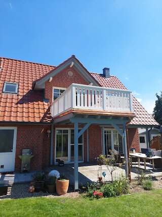 Weißer Holzbalkon mit Geländer und Stützkonstruktion an einem Backsteinhaus