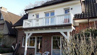Weißer Holzbalkon mit Holzgeländer über einer überdachten Terrasse an einem Backsteinhaus