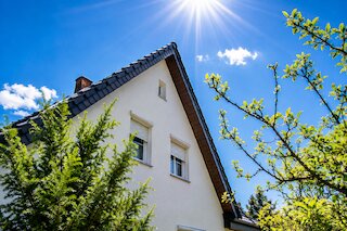 Weißes Wohnhaus mit steilem Satteldach, dunklen Dachziegeln und Fenstern im Giebelbereich