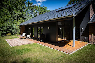 Überdachte Holzterrasse an einem dunkel verkleideten Wohnhaus