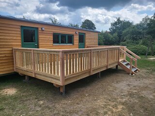 Holzterrasse mit Geländer und Treppe vor einem kleinen Holzhaus