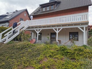 Erhöhter Holzbalkon mit weißem Geländer und Außentreppe