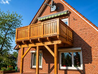 Großer Holzbalkon mit massivem Holzgeländer und Stützkonstruktion an einem Backsteinhaus