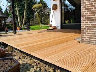 Große Holzterrasse mit gerillten Terrassendielen direkt am Wohnhaus und Blick in den Garten