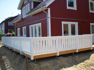 Holzterrasse mit weißem Geländer an einem roten Holzhaus