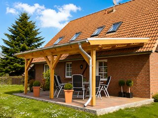 Terrassenüberdachung aus Holz an einem Backsteinhaus mit Sitzbereich und Garten